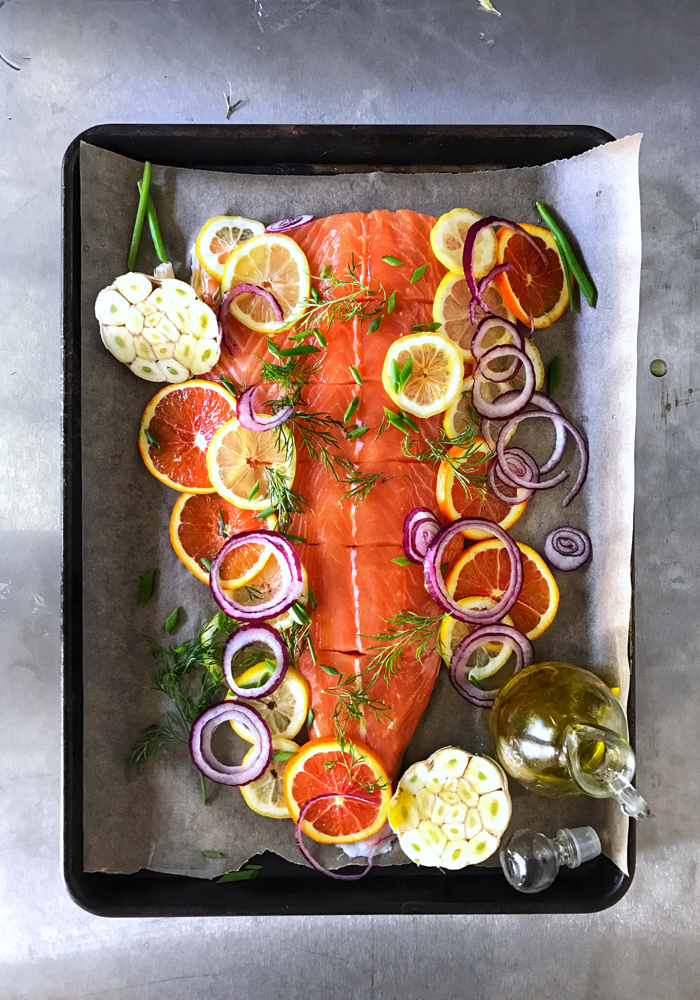 whole king salmon on baking sheet with citrus slice, garlic, herbs