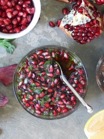 pomegranate salsa in glass bowl with poemgranate seeds and lemon wedges on side