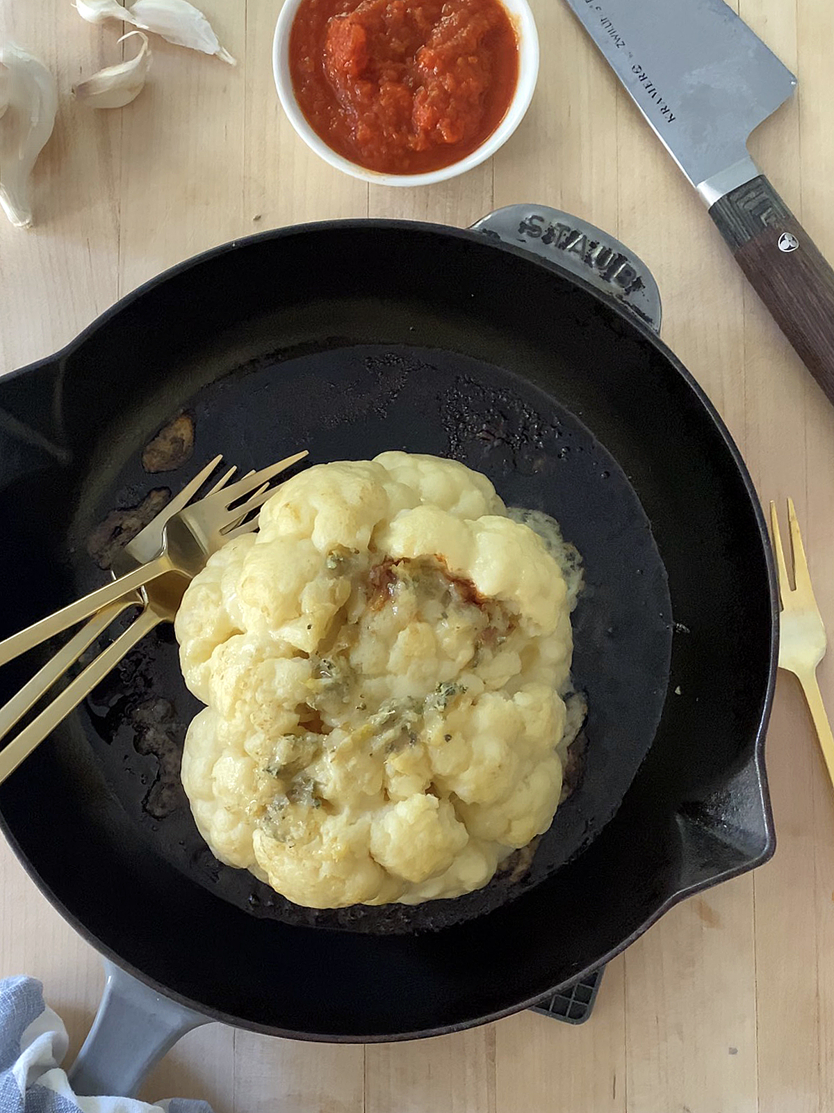 oven roasted whole cauliflower stuffed with cheese, in cast iron skillet on wooden cutting board background