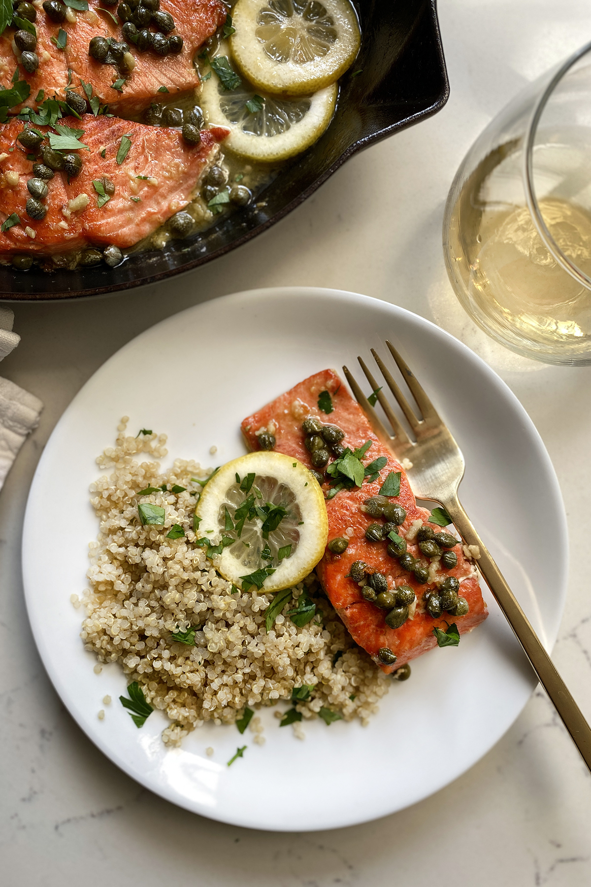 salmon piccata with lemon and capers, on white plate white plate with herb quinoa