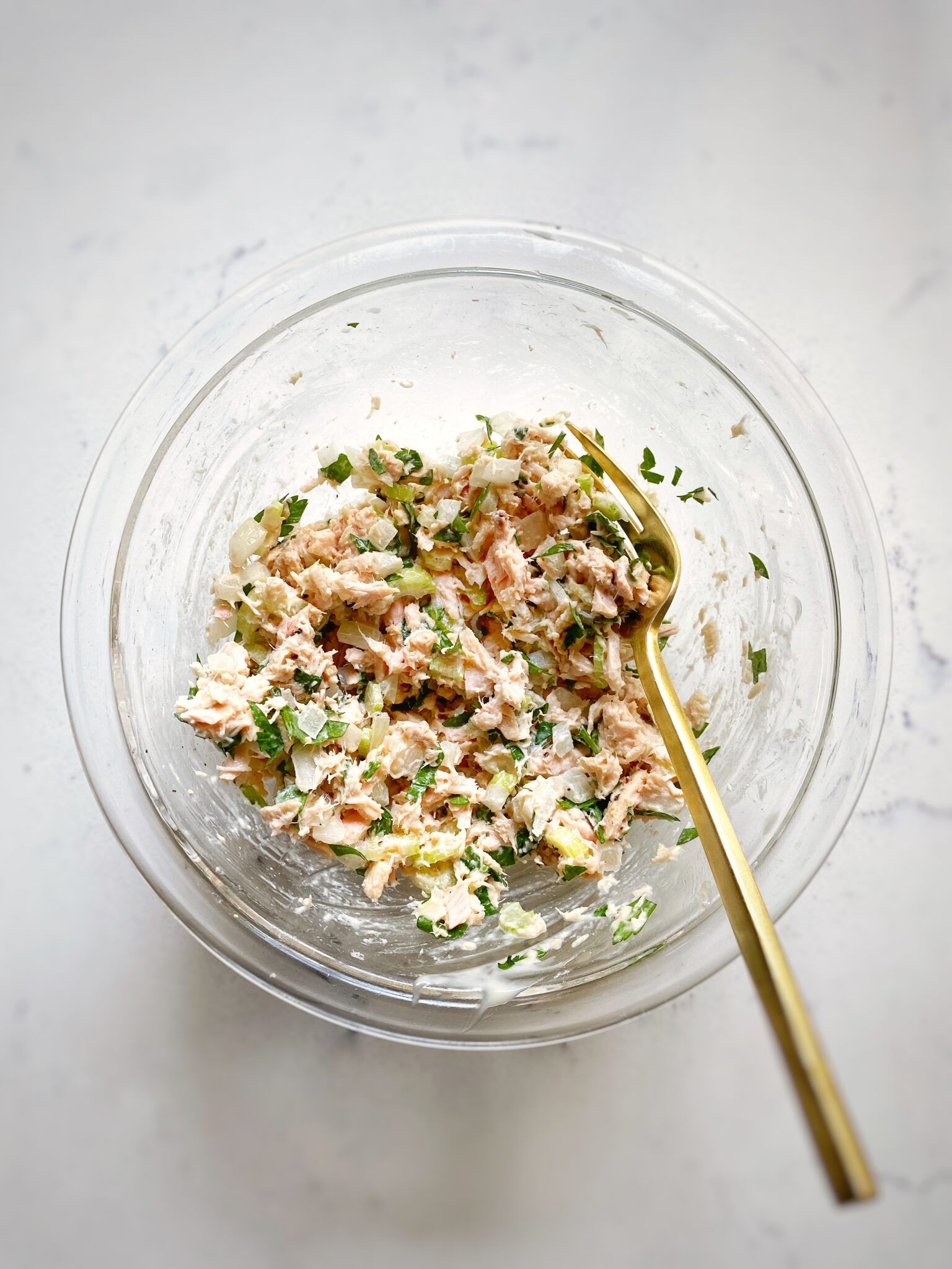 mixed tuna salad in glass mixing bowl on white marble background