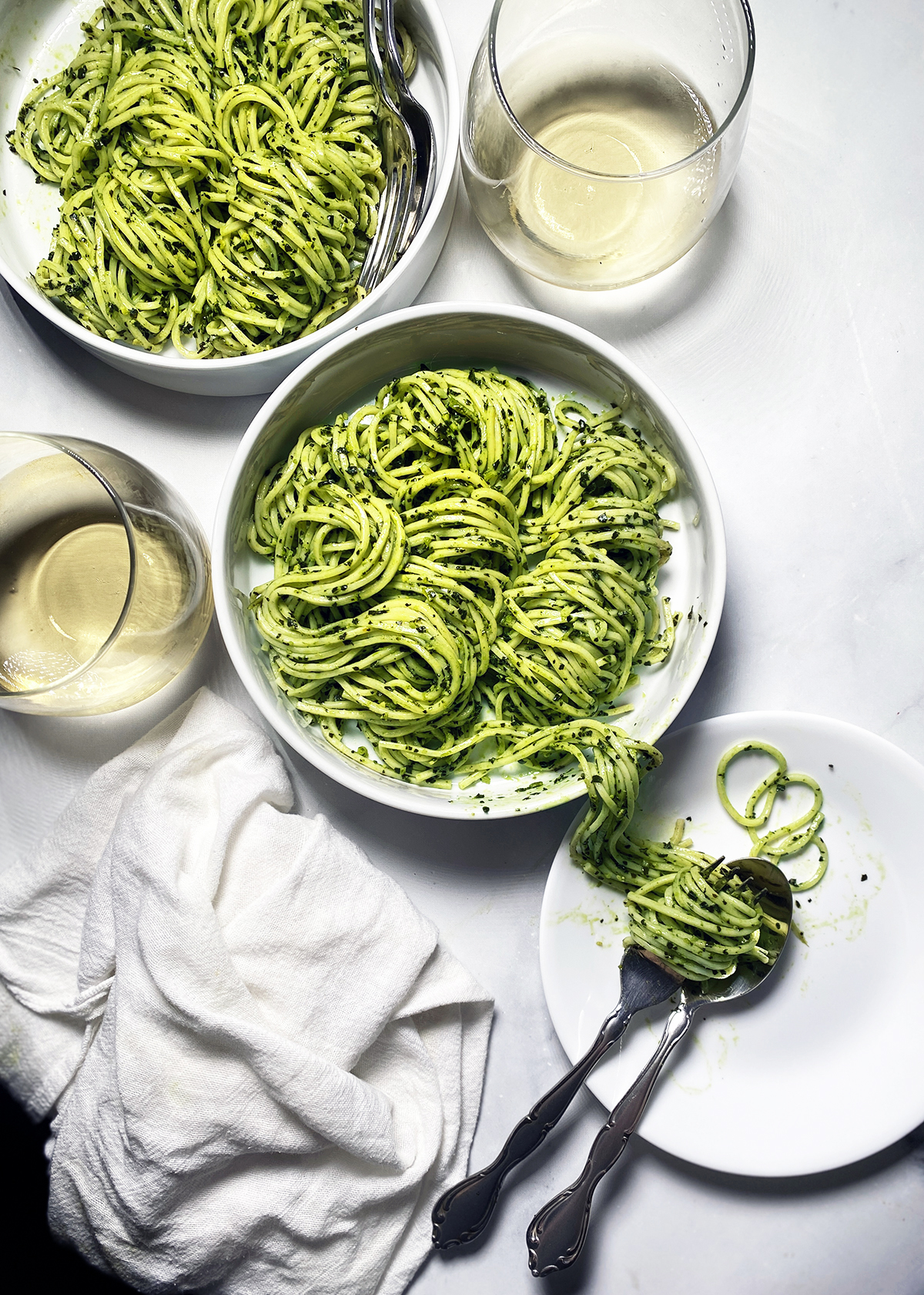 kale pesto pasta in white bowls and white wine in glasses on white tabletop