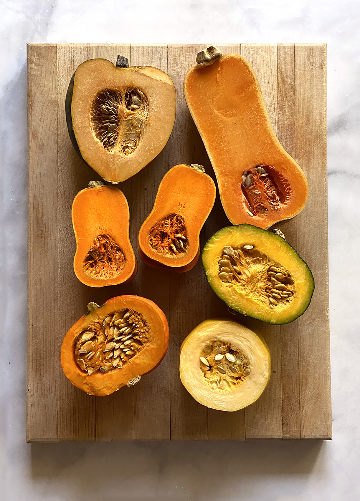 variety of winter squash cut open on wooden cutting board