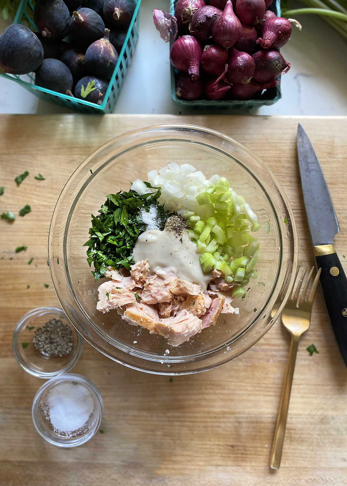 tuna salad ingredients in glass mixing bowl on wooden cutting board