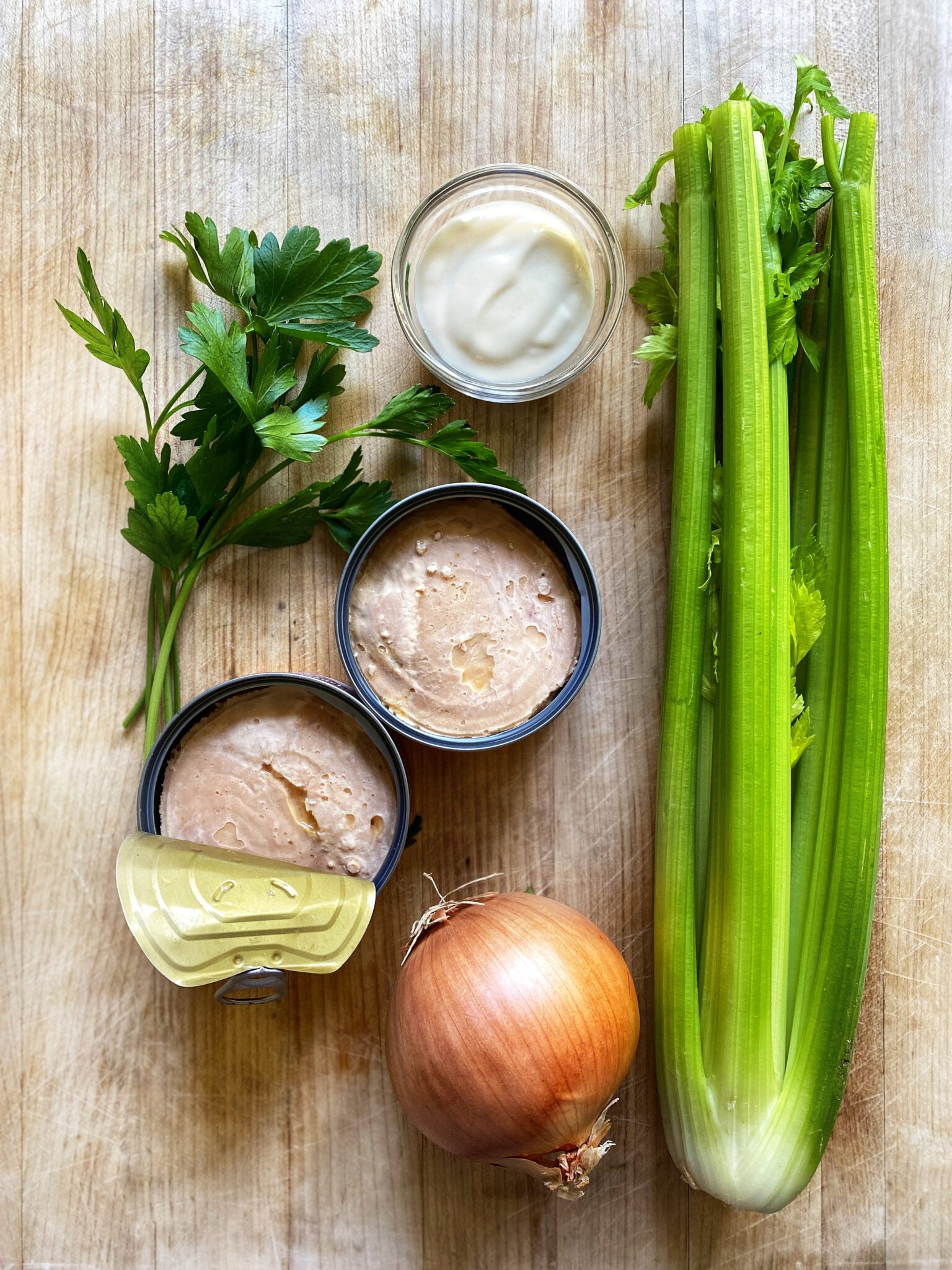 canned tuna mayonnaise celery onion parsley on wooden cutting board