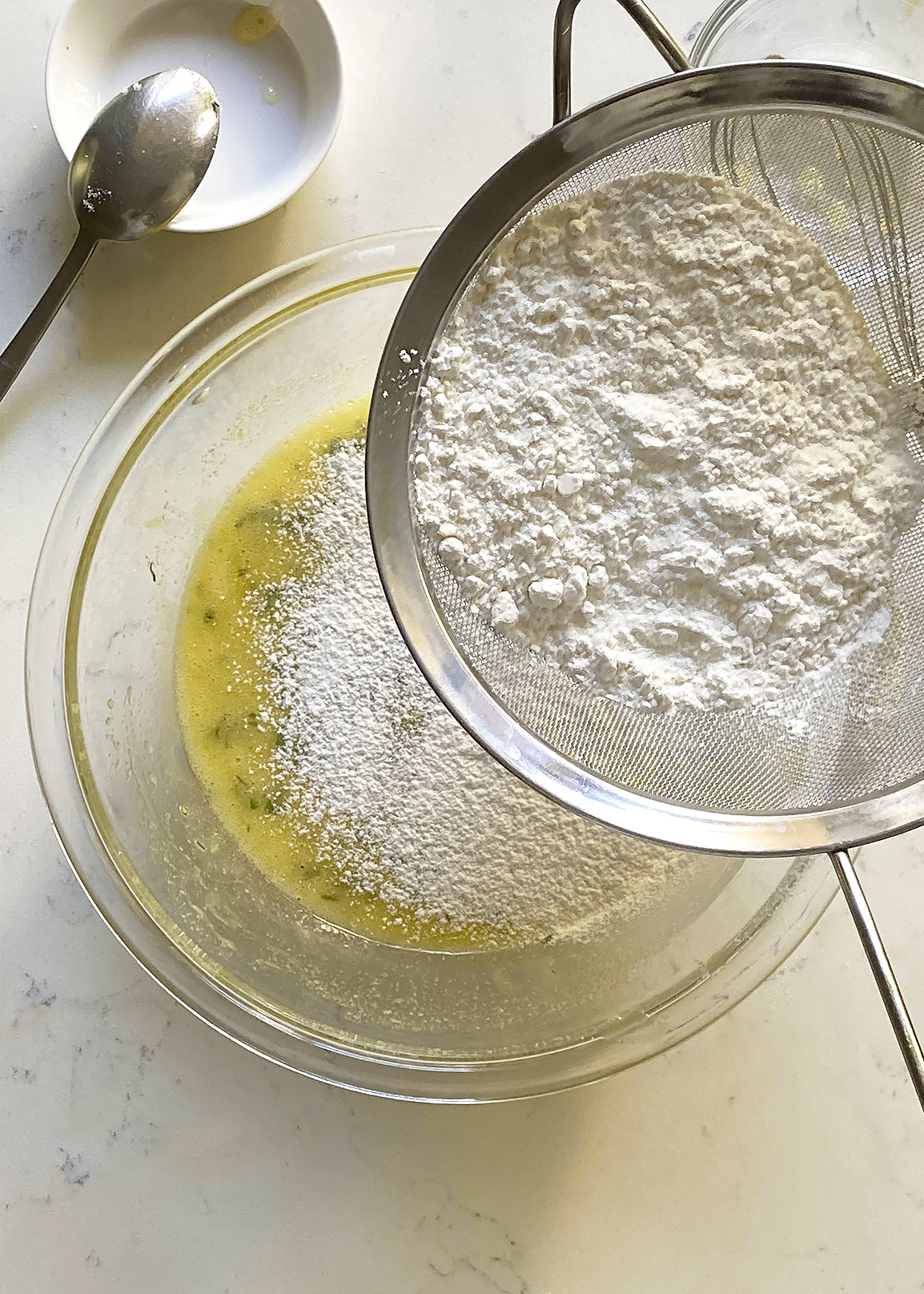 sifting dry flour ingredients into olive oil cake batter