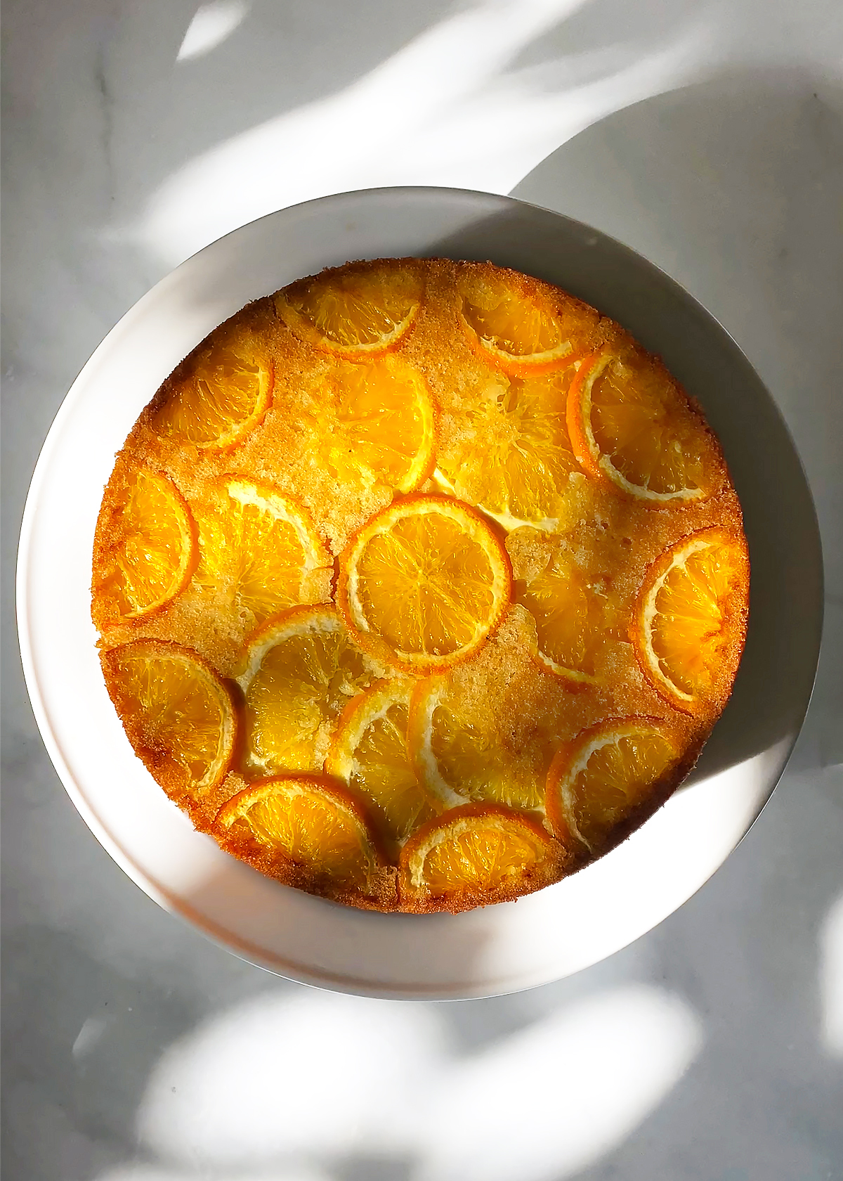 orange olive oil cake on white cake stand on marble countertop background