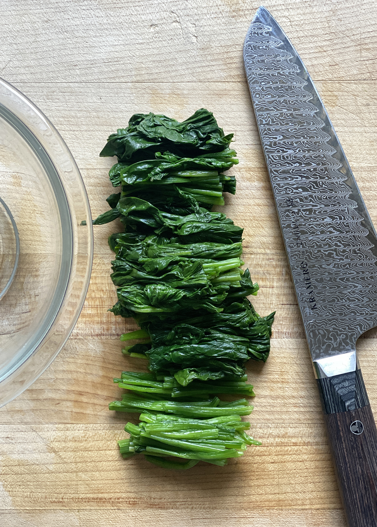 cooked spinach cut into 2-inch pieces lined up on wooden cutting board next to chef's knife