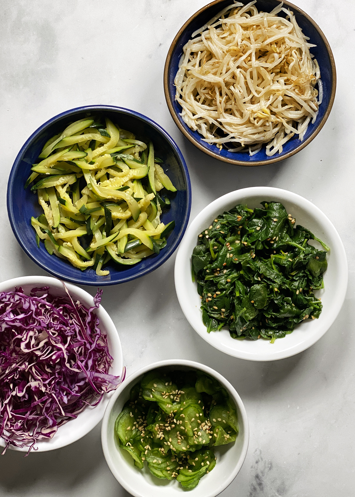 assorted korean vegetable banchans: bean sprouts, zucchini, korean spinach, red cabbage, pickled cucumber