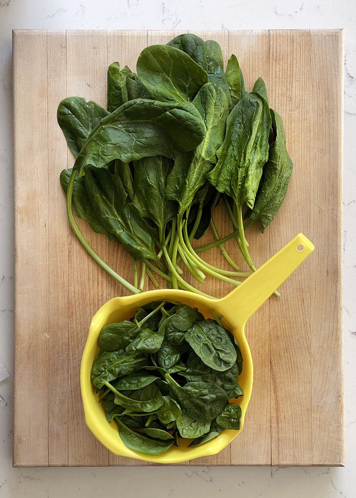 fresh large leaf spinach and yellow colander with baby spinach on wooden cutting board