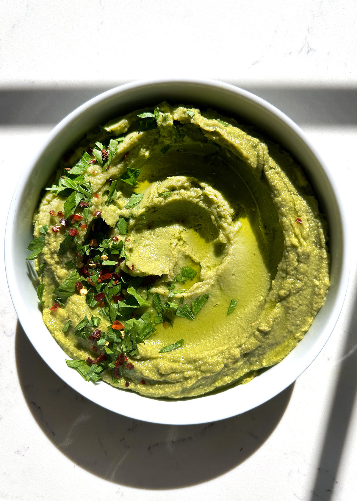 green avocado hummus garnished with parsley and crushed red pepper flakesin white sserving bowl