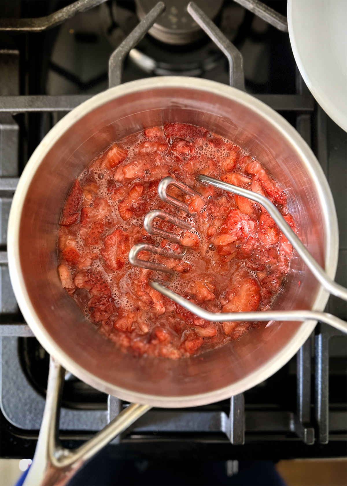 strawberries cooked and mashed in pot with potato masher