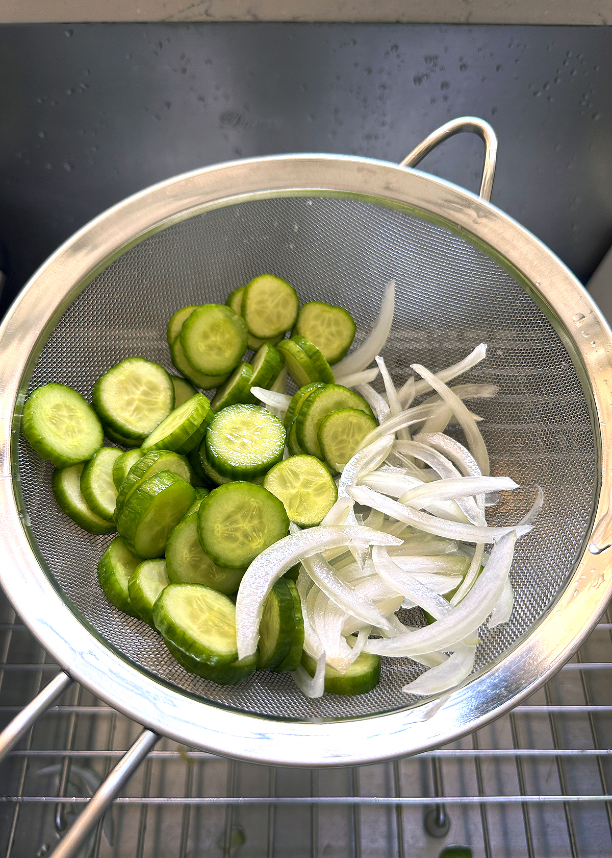 cucumbers and onions in sieve over sink, rinsed and drained