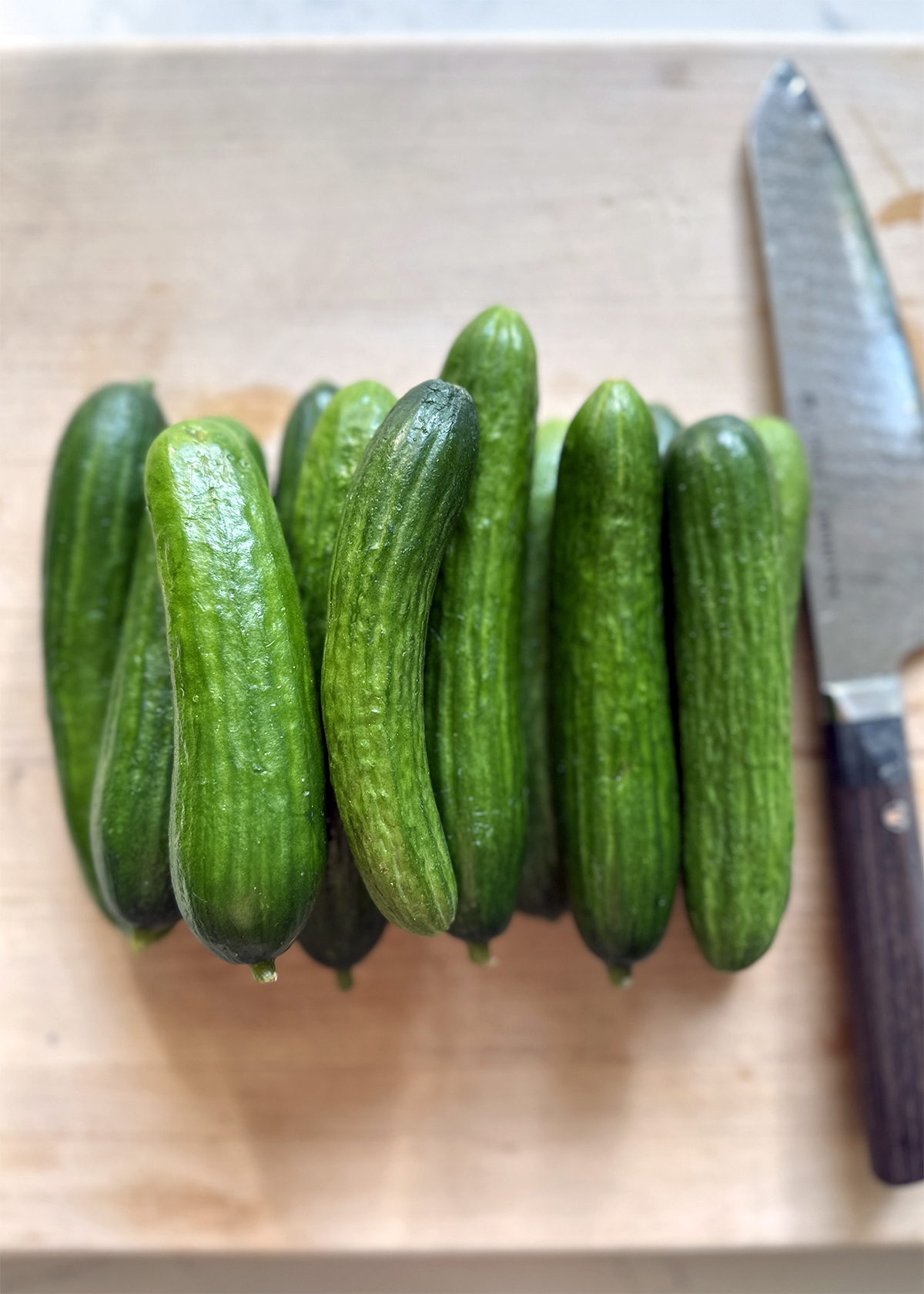 Persian cucumbers and large knife on wooden cutting board