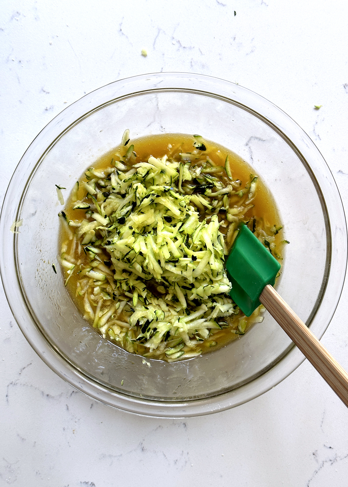 shredded zucchini added to wet ingredients, glass bowl