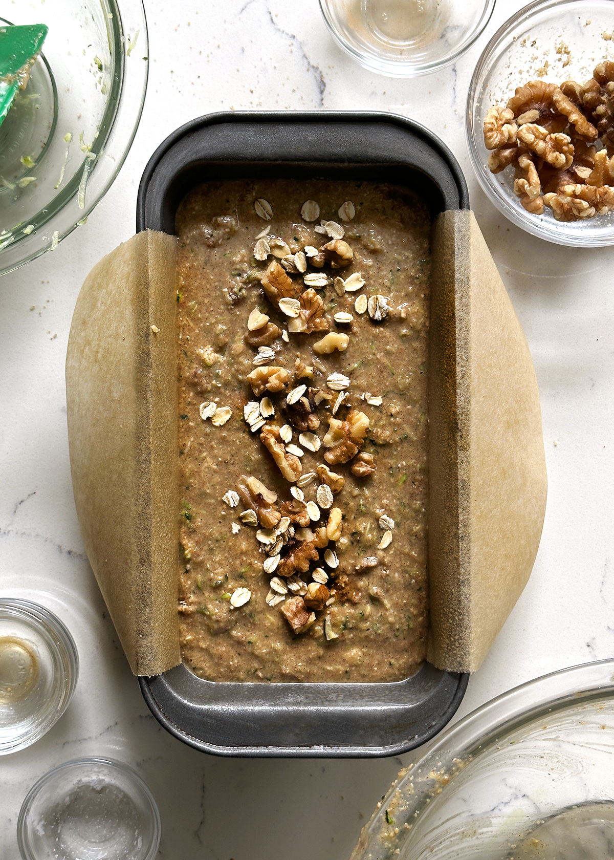 zucchini bread batter in loaf pan with walnuts, oats topping