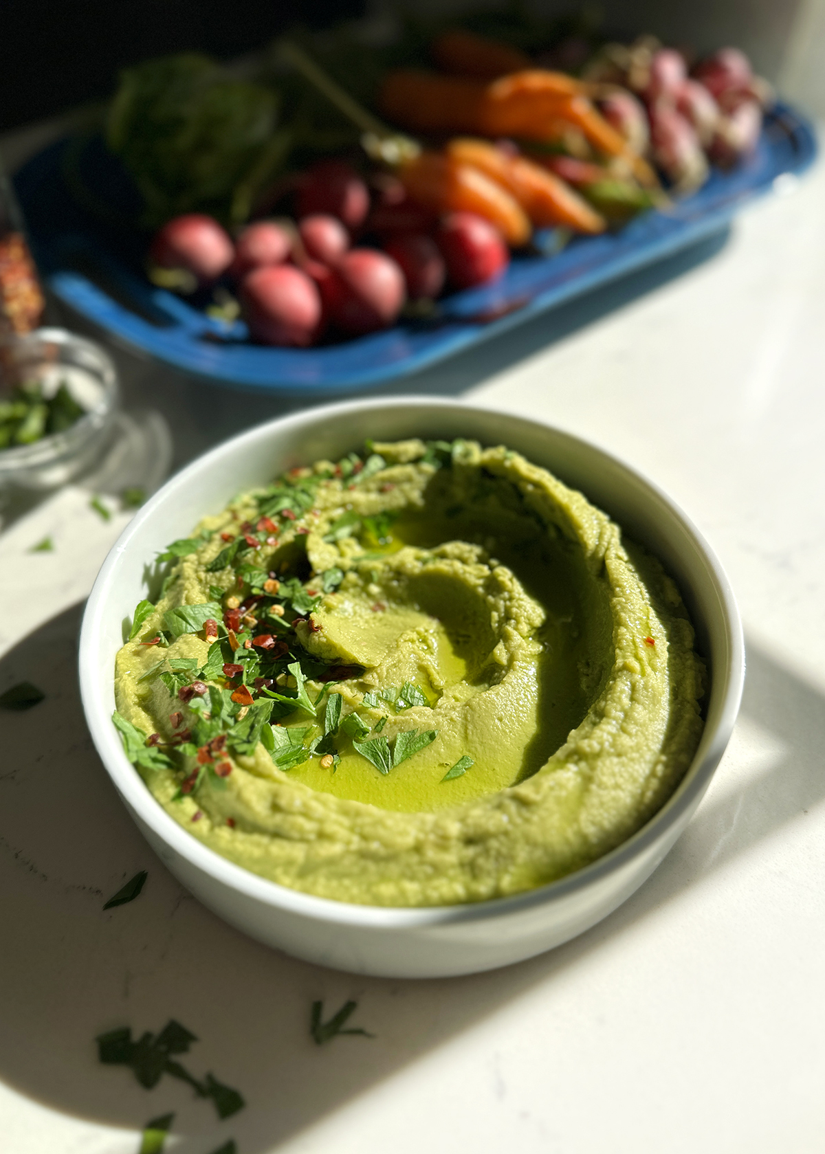 avocado hummus garnished with parsley and crushed red pepper flakes, in white serving bowl