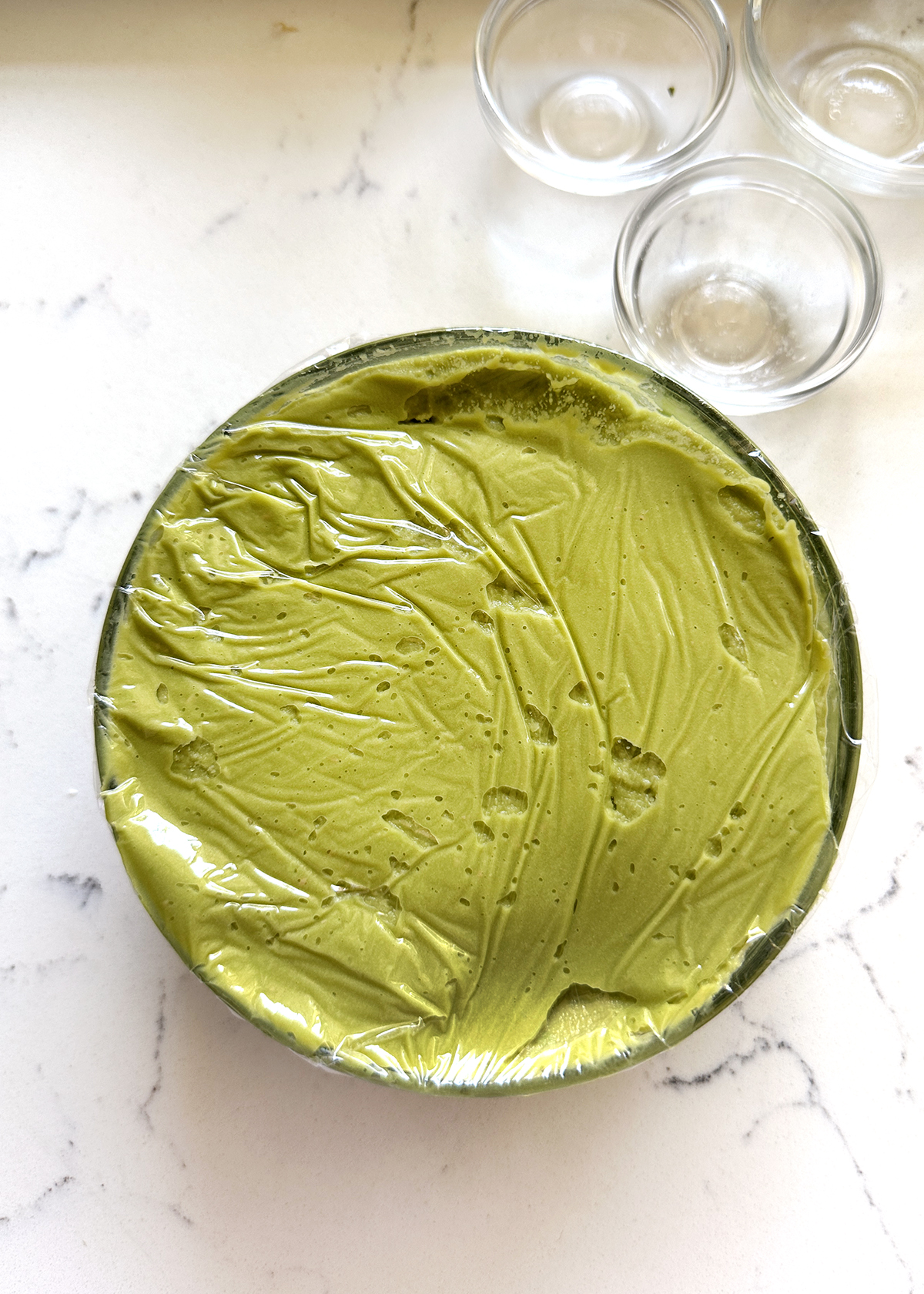 avocado hummus in glass bowl, wrapped in plastic