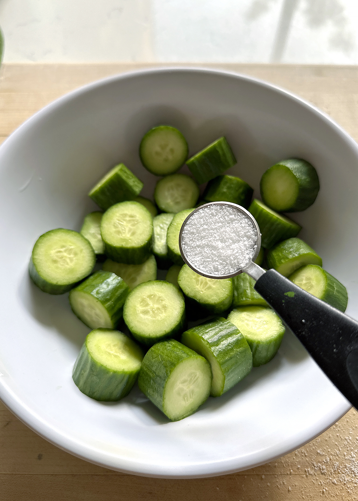 salt over sliced cucumbers in bowl