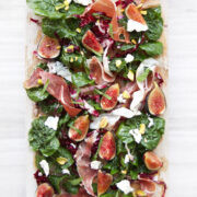 fig salad with arugula, prosciutto, and pistachios on wooden board