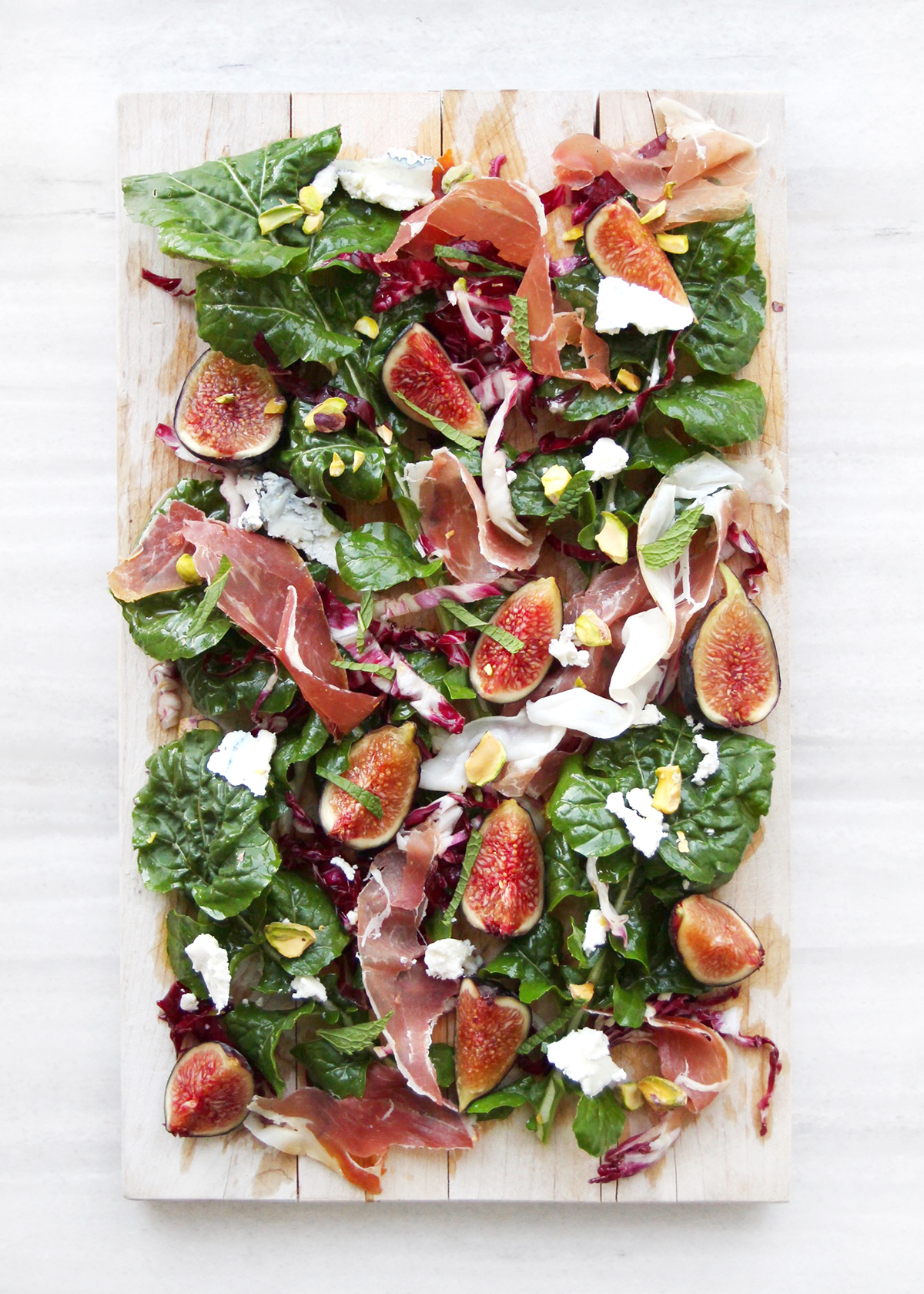 fig salad with arugula, prosciutto, and pistachios on wooden board