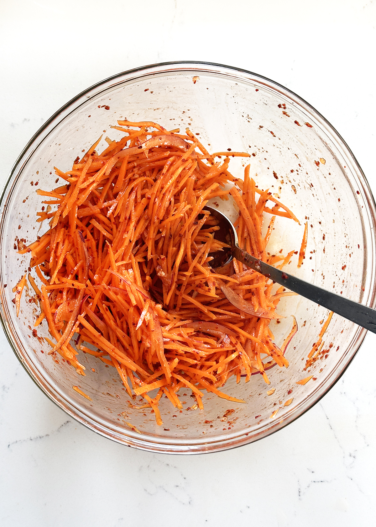 spicy carrot salad stirred in glass mixing bowl