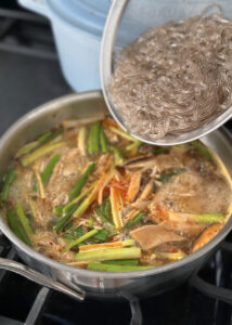 adding dang-myun glassy noodles to spicy soup